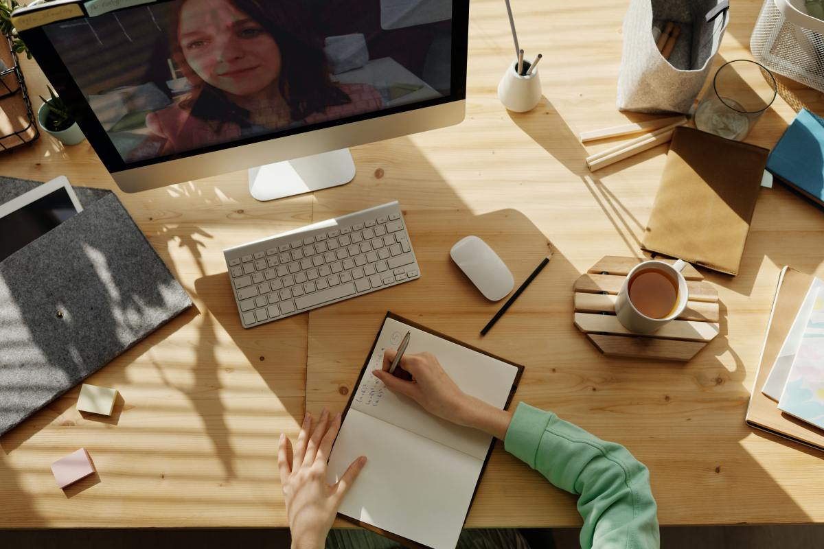 Woman surrounded by coffee, tablet, computer with video playing, notebooks and office supplies while taking notes.