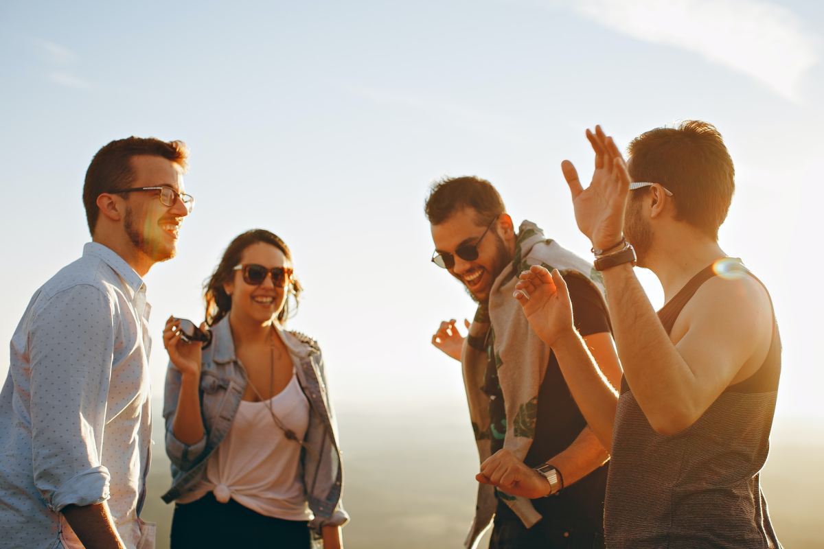 Three men and one woman smiling at the top of a mountain at sunset.